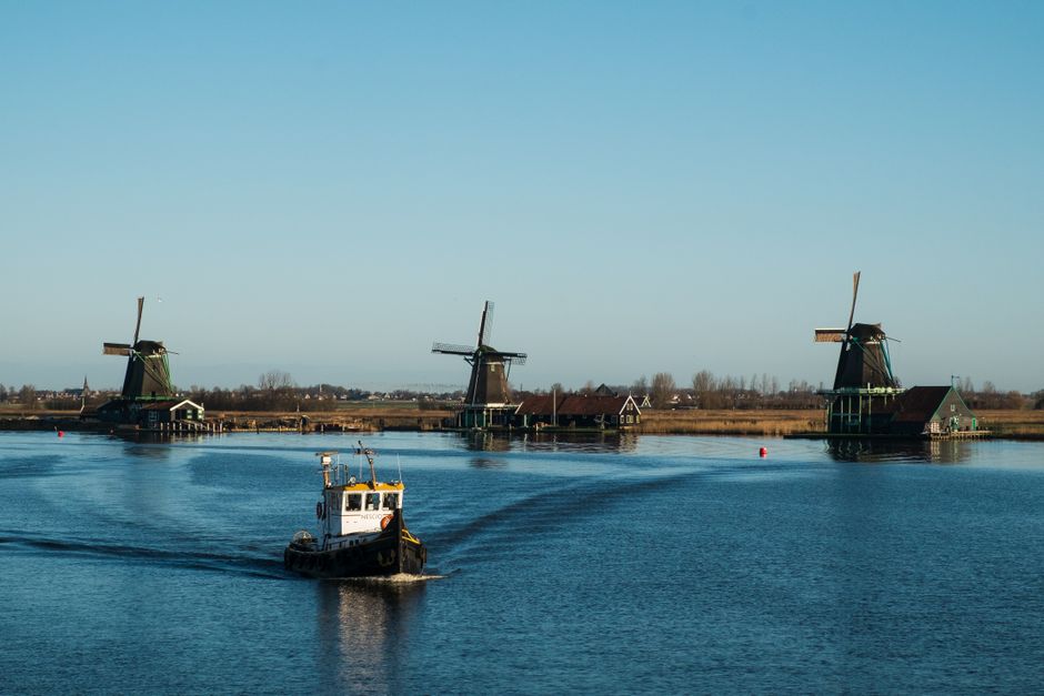 Traditional windmills and a boat on a calm waterway at Zaanse Schans in the Netherlands.