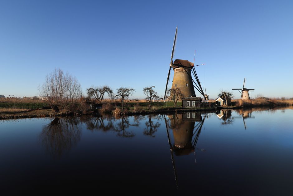 Historic windmills mirrored on a calm river under a clear blue sky in Kinderdijk, Netherlands.