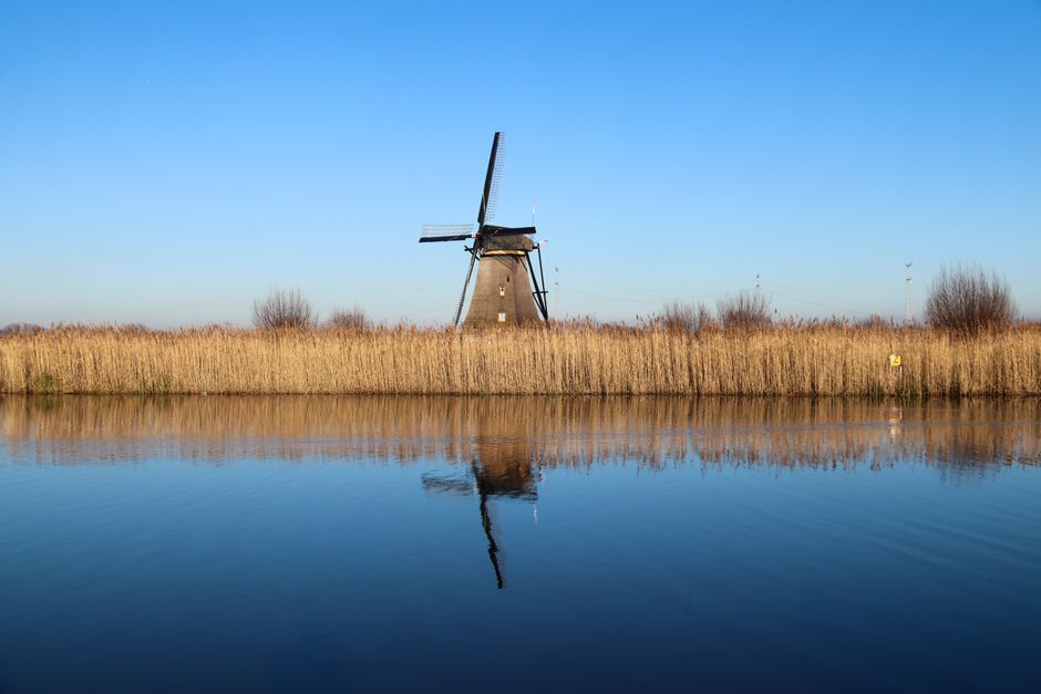 Scenic view of a windmill reflecting on a calm canal in Kinderdijk, Netherlands.